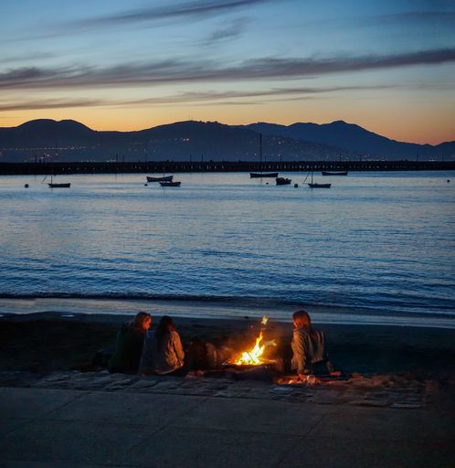 A scenic view of people sitting around a bonfire on the beach during a late sunset