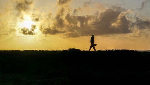 A scenic view of a hiker walking on a field during a vibrant sunset in the sky