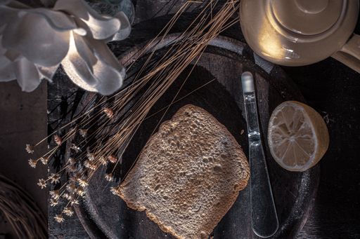 A top view of a toast on a tray on the table with a teapot and artificial flowers on it
