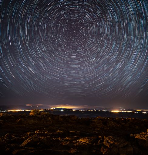 A town surrounded by lights in the evening under a starry sky with long exposure