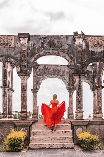 A vertical shot of a woman in a red dress walking up stairs of Taman Soekasada Ujung. Bali, Indonesia.