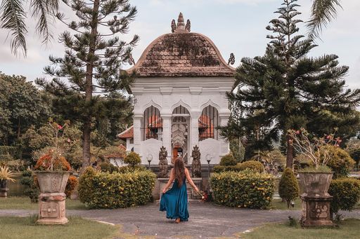 A young female in a blue dress holding flowers in Water Palace Soekasada Taman Ujung Ruins on Bali Island in Indonesia