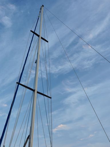 A vertical shot of a yacht mast on the background of the sky