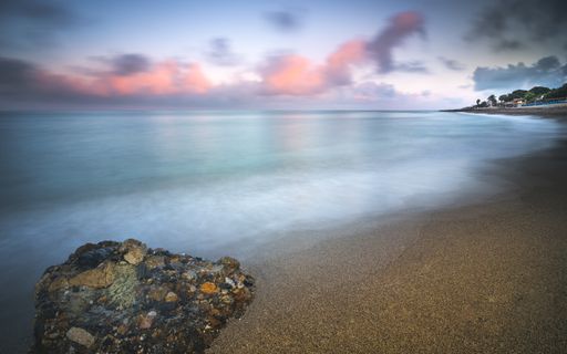 A scenic view of the seashore with misty water effect and colorful sky during twilight