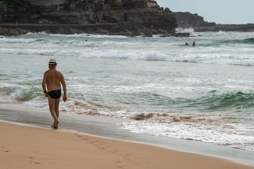 The man with a hat walking along the sandy shore.