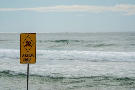 A sign with text: dangerous current, against the background of the sea.