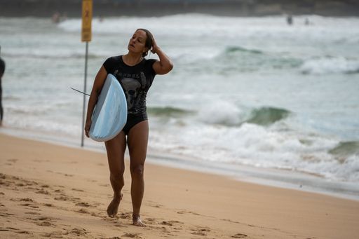 The woman with a surfboard walking along the sandy shore. Manly Beach, Australia.