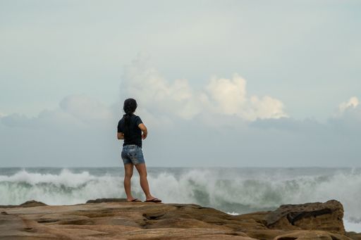 The girl standing on the edge of the cliff and looking at the ocean waves.
