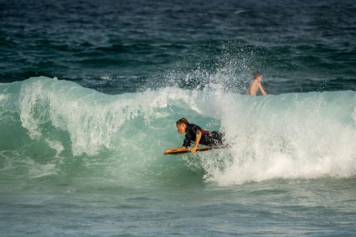 A surfer catching a wave at the beach on a sunny day at Manly Beach, Australia.