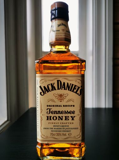 A vertical closeup of a bottle of Jack Daniels Tennessee Honey on the table with the window background
