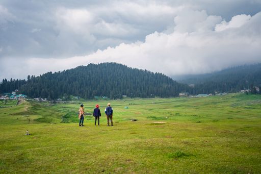 A shot of three people standing on a grass field surrounded by hills