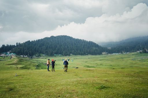 A shot of three people standing on a grass field surrounded by hills