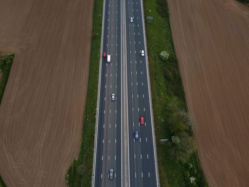 An aerial shot of a highway surrounded by green trees and adry sandy land