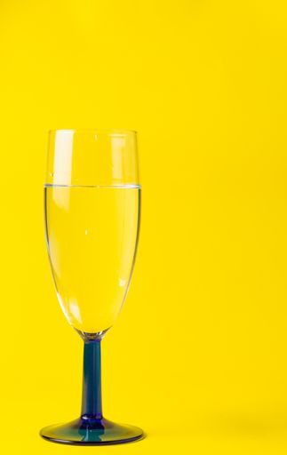 A vertical sot of a wine glass with clear water against a yellow background