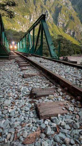 A vertical shot of train tracks near cliffs with an illuminated train approaching