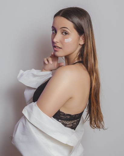 A vertical shot of a female in lingerie and a white shirt with moisturizing cream on her face - perfect for a spa concept