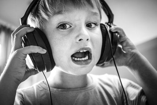 A closeup grayscale of a young boy wearing headphones, looking into the camera with a contemplative expression