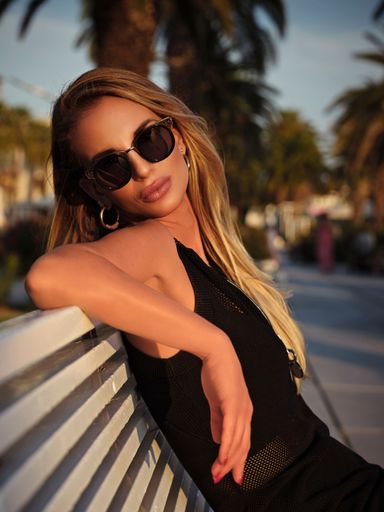 A vertical shot of a sexy young female with sunglasses posing on a bench