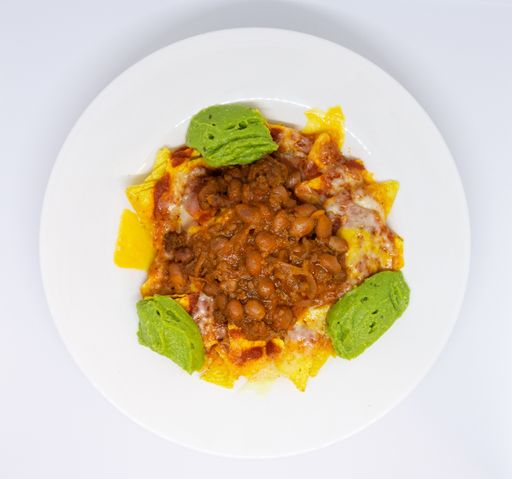 An overhead shot of a late of nachos combined with guacamole and meat on a white surface