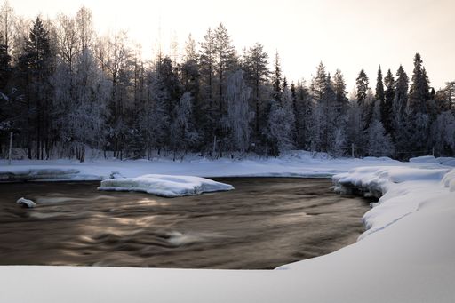 A beautiful view of a river in a frozen and snow-covered land with a forest in the background