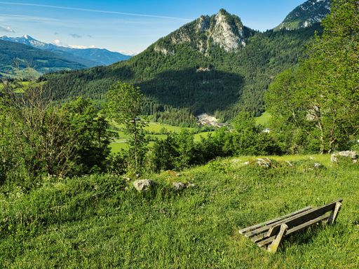 A wooden bench on a green hill with a view of Grimming peak in Purgg village, Styria, Austria