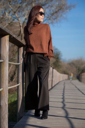 A vertical closeup portrait of a Hispanic female standing on a wooden bridge while wearing a casual outfit