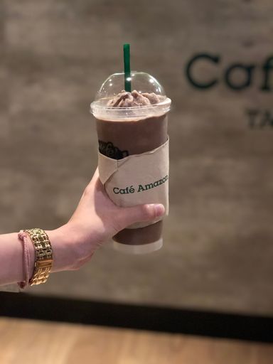 A vertical closeup of a hand holding chocolate frappe.