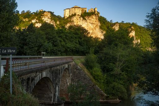 A beautiful shot of a bridge leading to a tree-covered hill with a castle in Bruniquel ,France