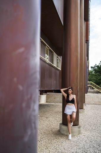 A vertical shot of young caucasian female posing while leaning on a column of a building