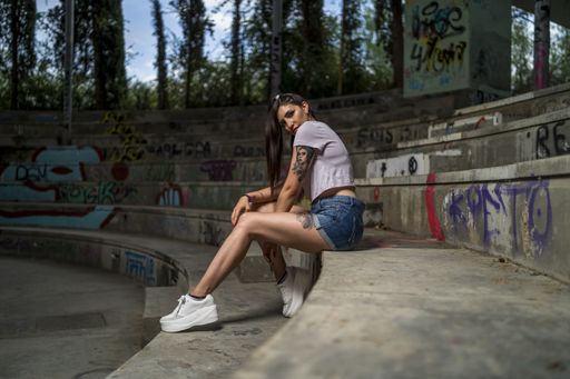 A young caucasian tattooed female in shorts posing while sitting on the stairs with graffitis