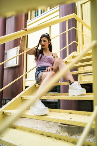 A vertical shot of a young rebellious caucasian female with tattoos and in jeans skirt posing while sitting on the yellow stairs