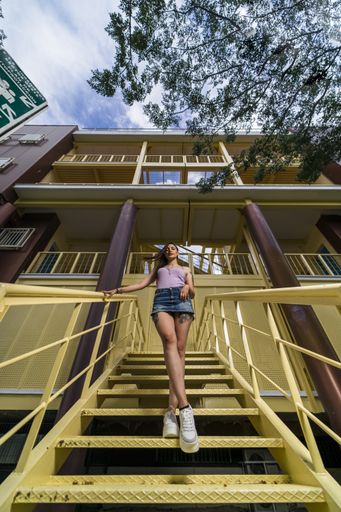 A vertical low angle shot of a young caucasian female posing while standing on the yellow stairs of a building