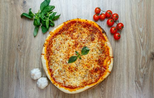 A top view of pizza margherita with cherry tomatoes,greens and garlic besides on a wooden table