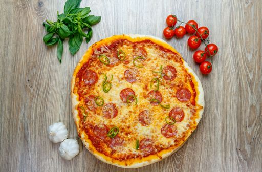 A top view of Pizza Diavola with salami, mozzarella, green hot pepper with ingredients next to it on a wooden table