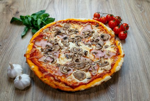 A top view of Pizza capricciosa with cherry tomatoes,greens and garlic on a wooden table