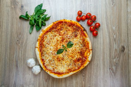 A top view of pizza margherita with cherry tomatoes,greens and garlic besides on a wooden table
