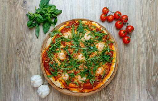 A top view of pizza margherita with cherry tomatoes,greens and garlic on a wooden table