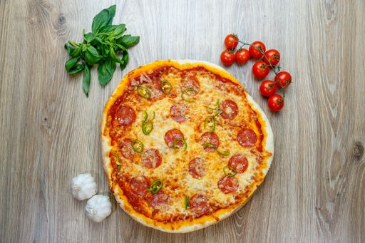 A top view of Pizza Diavola with salami, mozzarella, green hot pepper with ingredients next to it on a wooden table