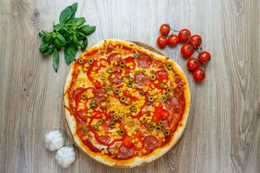 A top view of a pizza with pepperoni, tomato, olives and corns on a wooden table