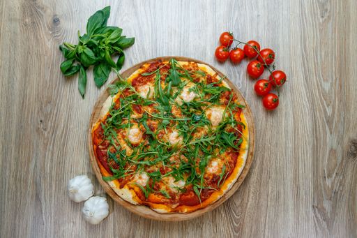 A top view of a pizza with tomato sauce, cheese and arugula on a wooden table