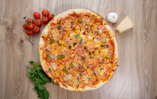 A top view of a gourmet tomato pizza on a wooden table with ingredients