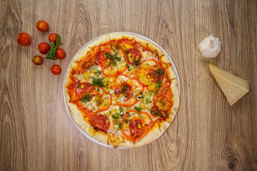 A top view of a gourmet vegetable pizza on a wooden table with ingredients