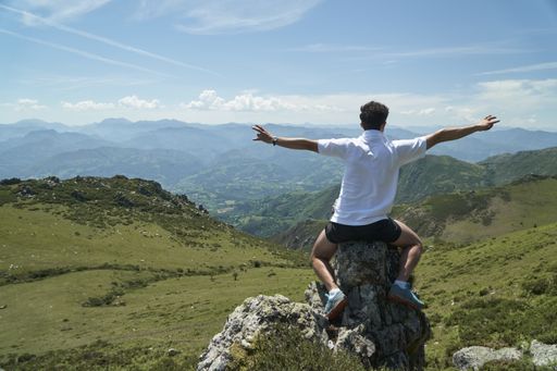 A young male sitting on a rock with open arms surrounded by hills covered in greenery
