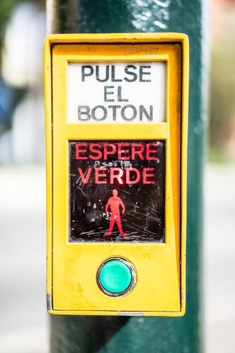 A vertical closeup shot of a sidewalk crossing button with spanish text
