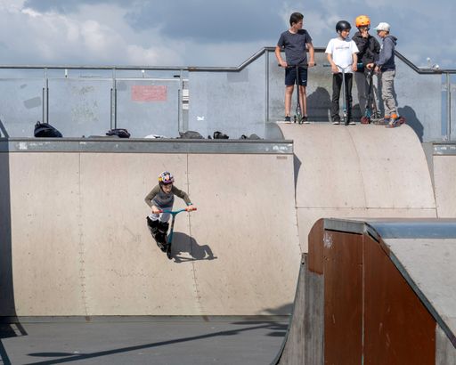 The young kids on scooters performing tricks on the ramp