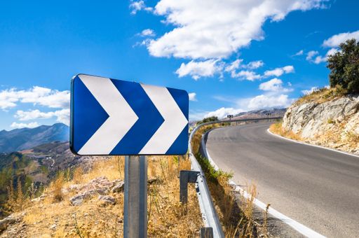 A blue white street sign showing directions next to a road with a scenic background