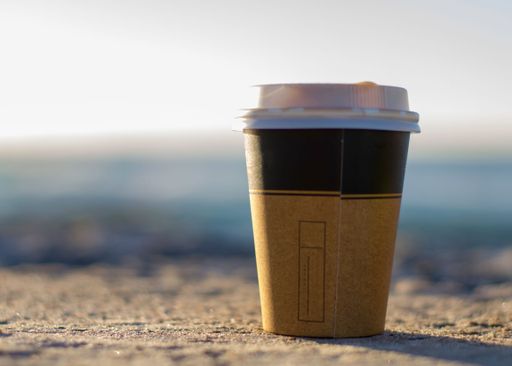 A closeup of a paper takeaway cup on a sandy beach