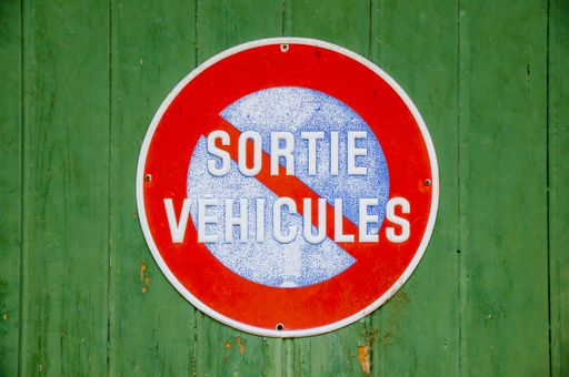 A round red blue no parking street sign with french text on a green surface