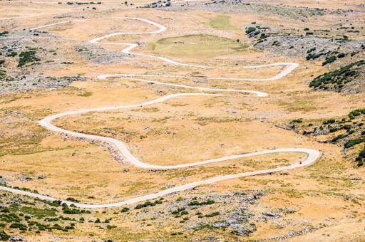 An aerial shot of a long curvy road leading through dry land