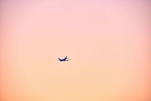 A beautiful shot of an airplane flying high up in a pink sky at sunset in Stanley